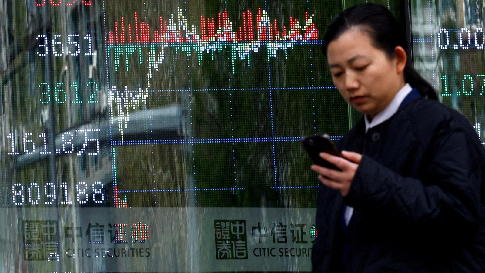 Una dona xinesa junt a un panell que mostra informació sobre l'índex borsari, a Pequín, la Xina