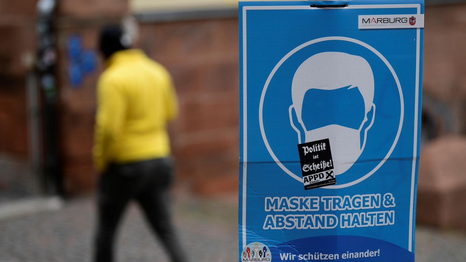 Un vianant passa un cartell que recorda l'obligatorietat de la mascareta a Marburg, Alemanya