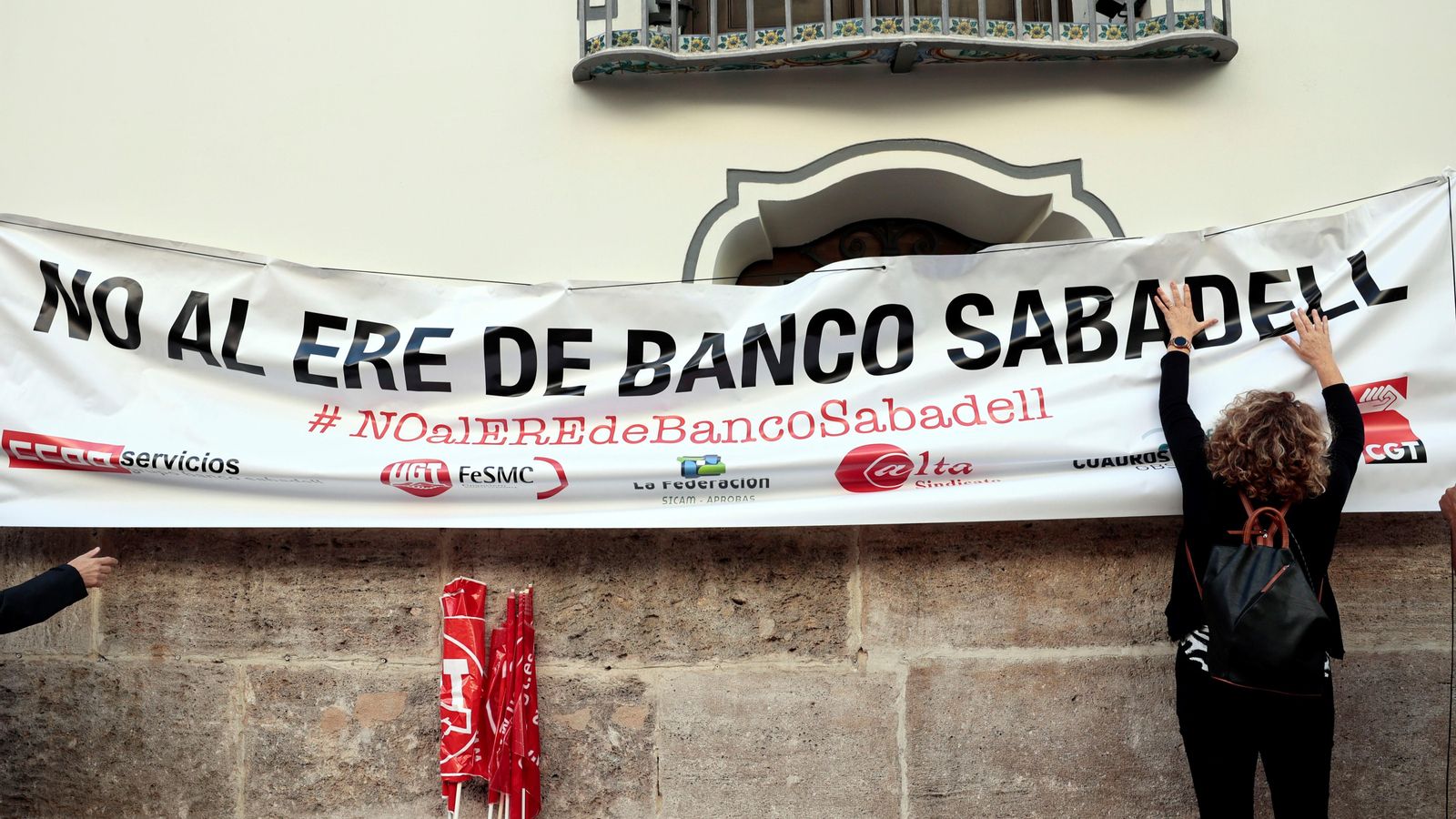 Una persona penja una pancarta en la façana del banc Sabadell a València