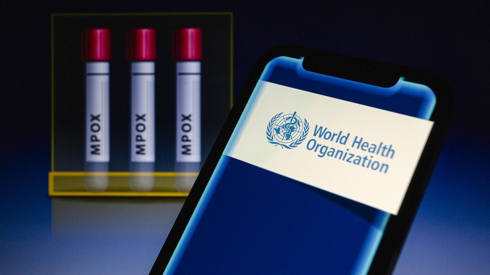 Logo de l'OMS en la pantalla d'un telèfon, davant d'una representació gràfica amb tres tubs de mostres d'mpox