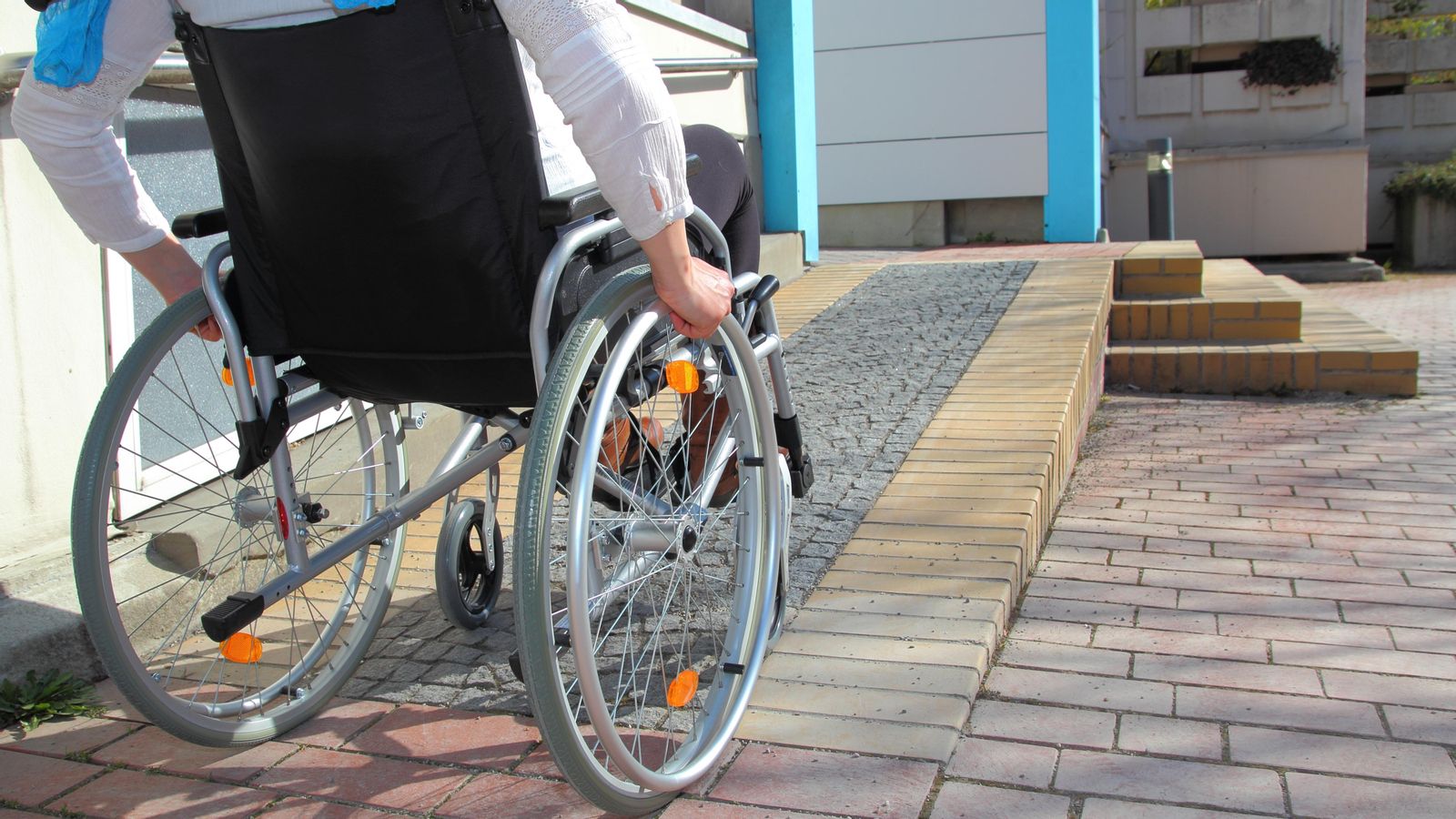Una persona en cadira de rodes fa servir una rampa per a accedir un edifici