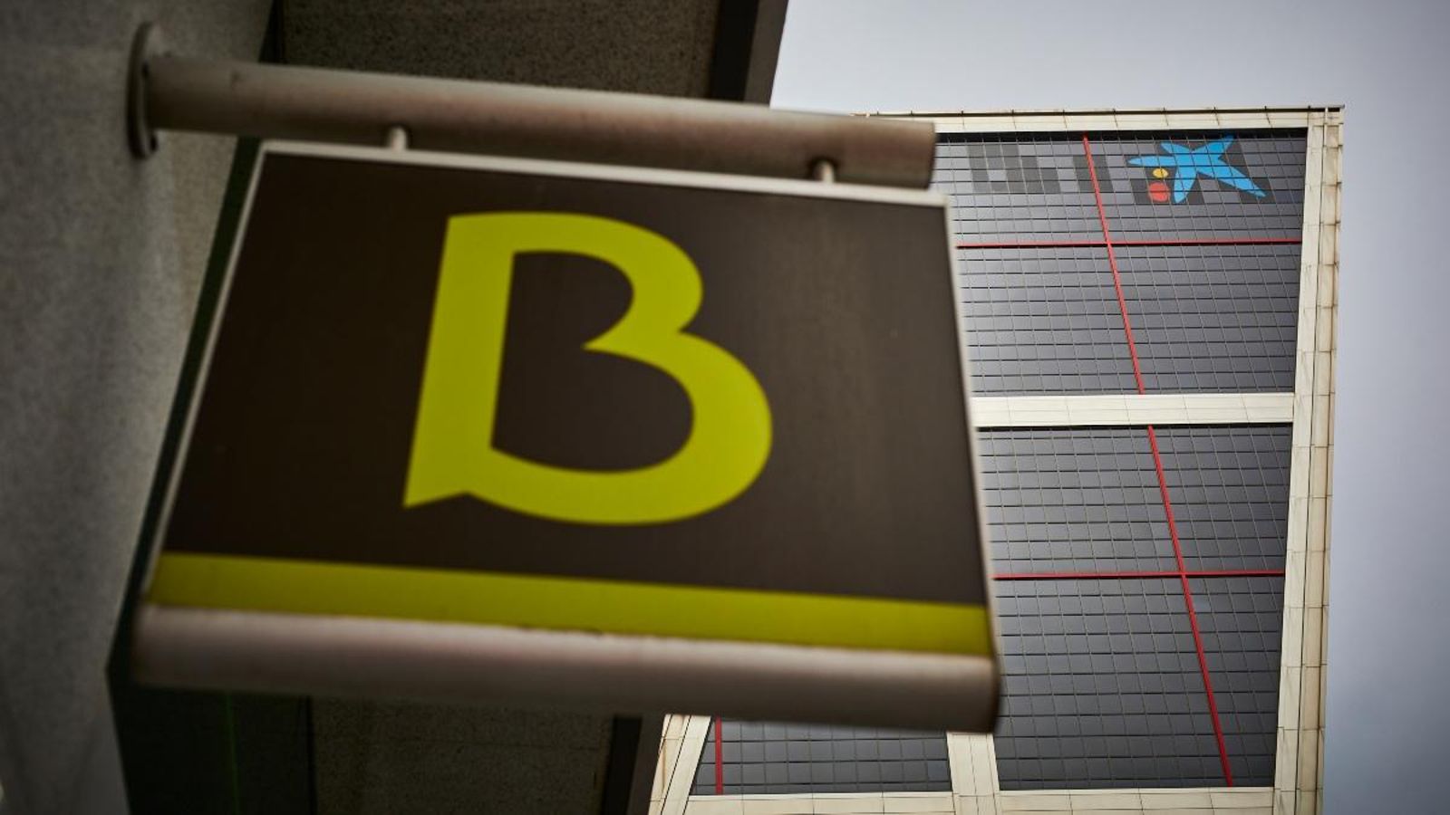 Cartell amb el símbol de Bankia amb el logo de CaixaBank de fons, que l'ha substituït a les Torres Kio de Madrid
