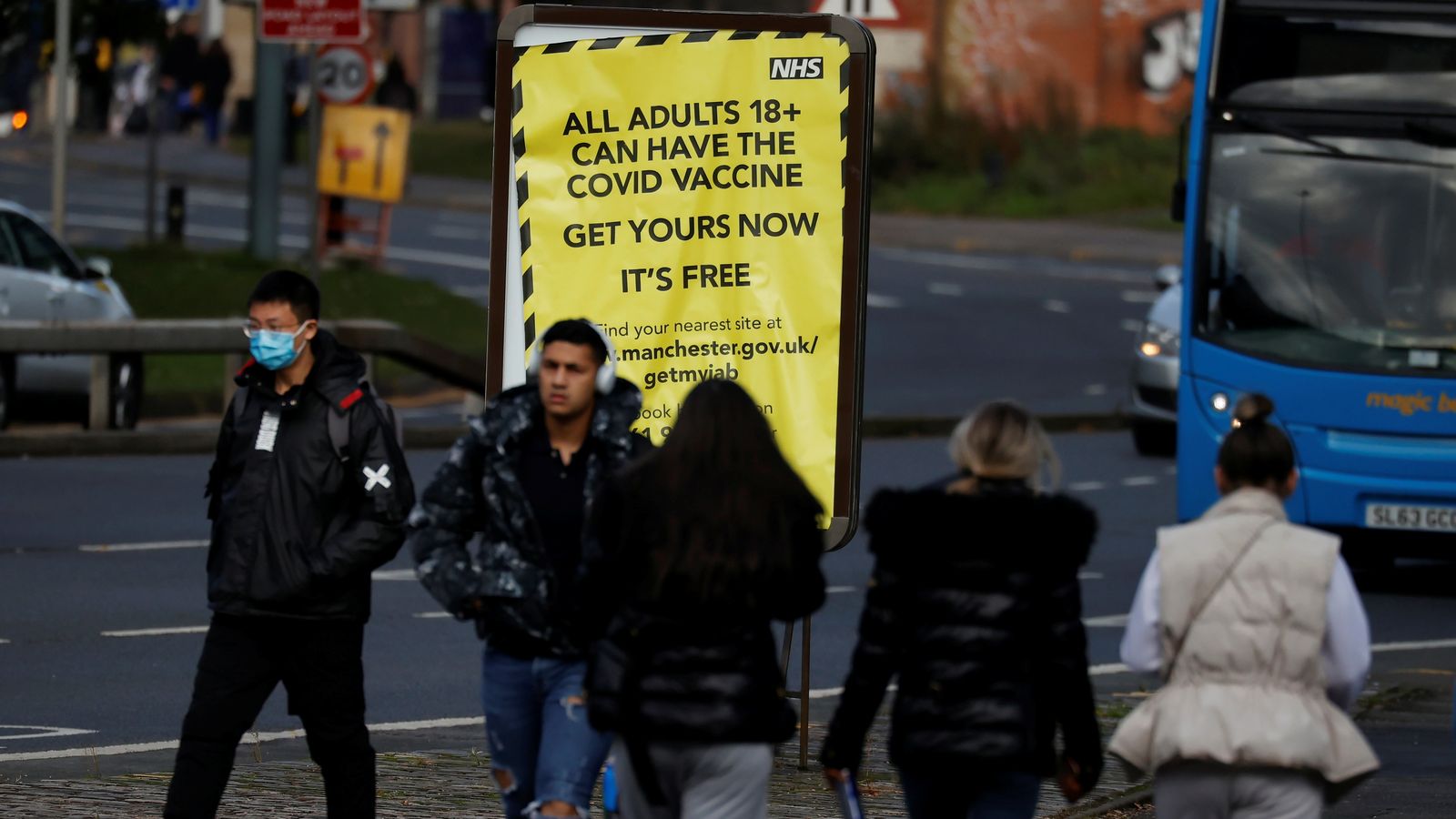 Diversos vianants passen per davant d'un cartell a Manchester que crida a la ciutadania a vacunar-se a
