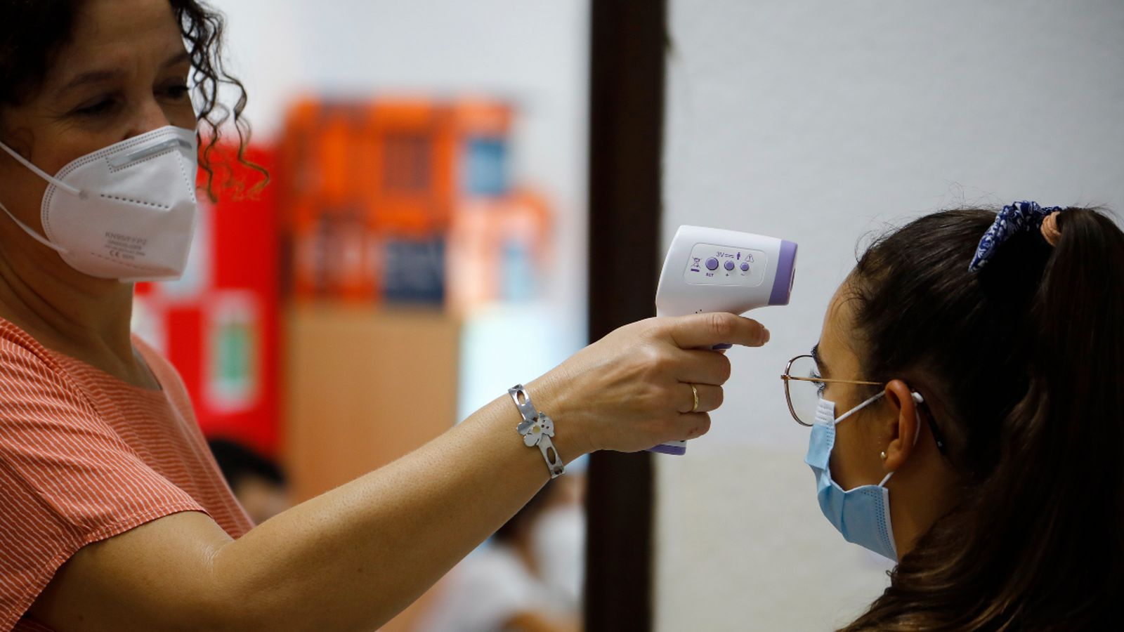 Una mestra pren la temperatura a una xiqueta a l'entrada de l'escola