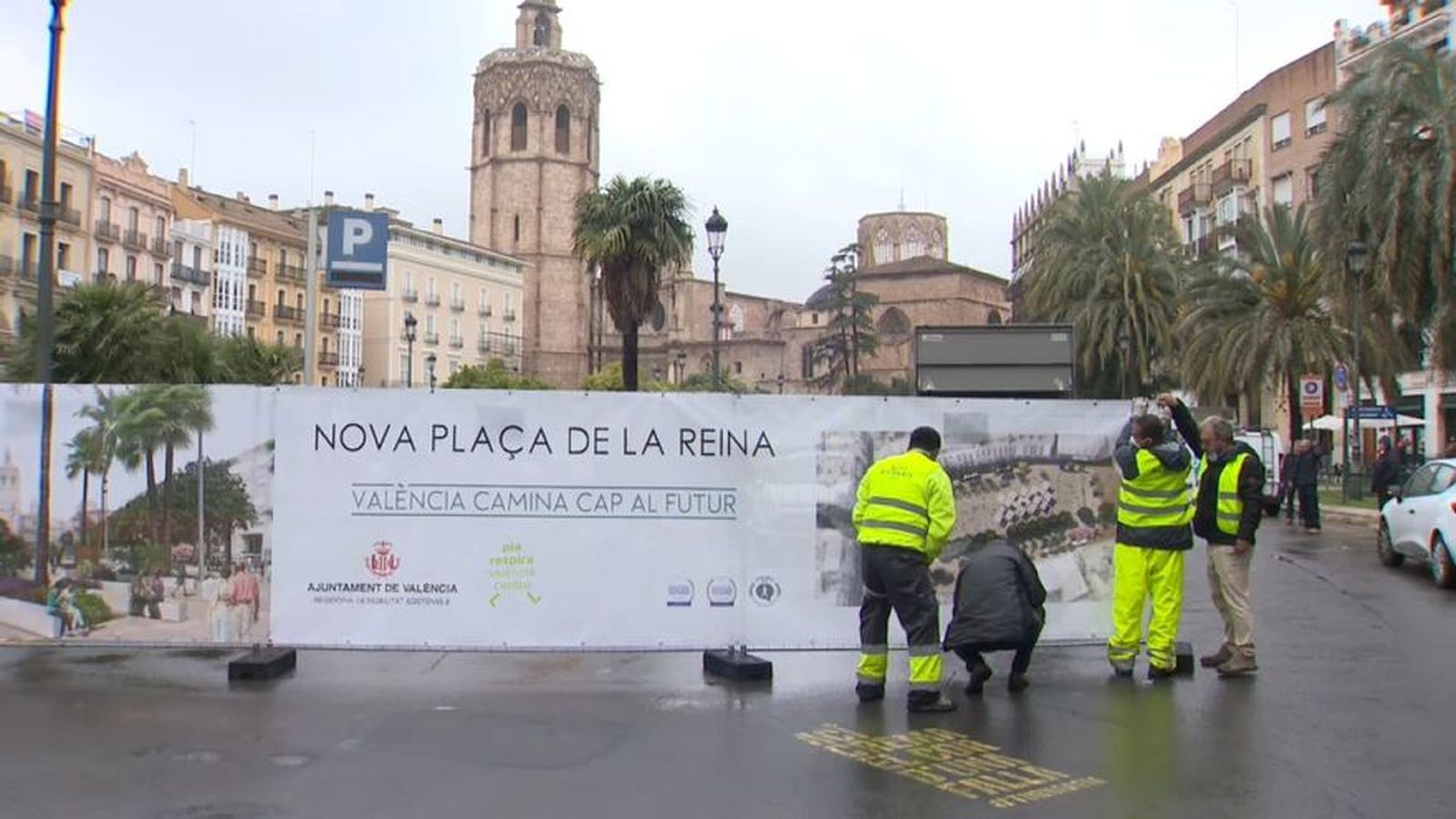 Uns operaris alcen el cartell que informa de les obres de la Plaça de la Reina