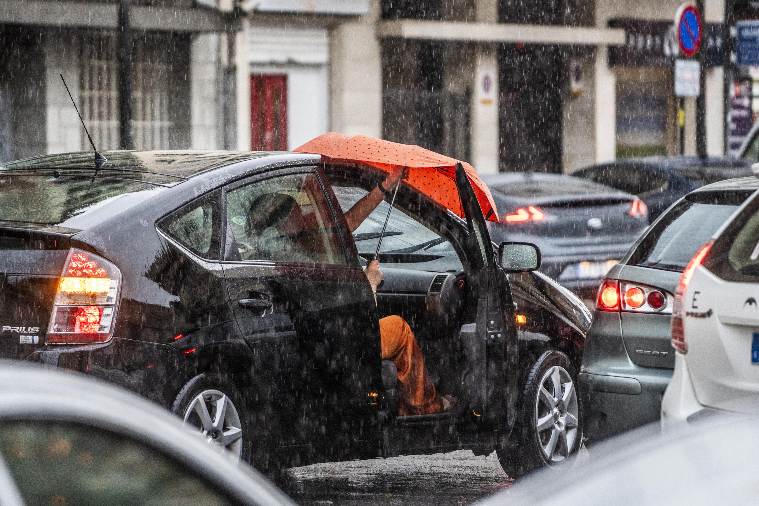 Un home puja al vehicle enmig de la plutja