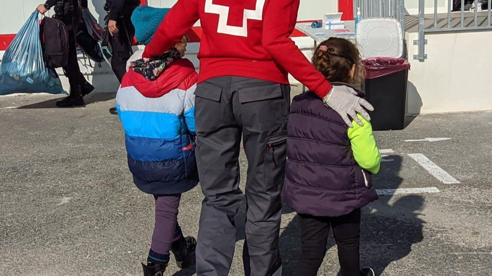 Un dels sanitaris de la Creu Roja acompanya dos dels menors que viatjaven en la pastera