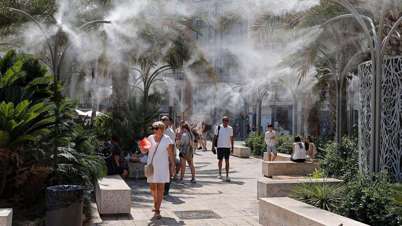 Turistes es refresquen amb els aspersors de la plaça de la Reina a València, este divendres