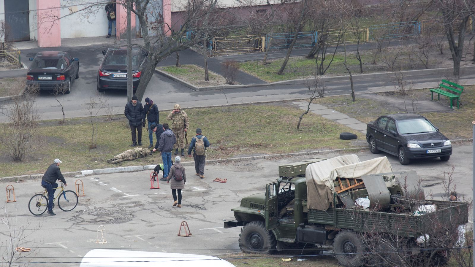 Un grup de persones envolta un soldat abatut al costat d'un vehicle militar en una zona residencial de Kíev