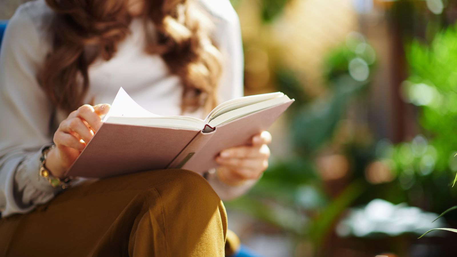Una jove llig un llibre a un parc, en una imatge d'arxiu