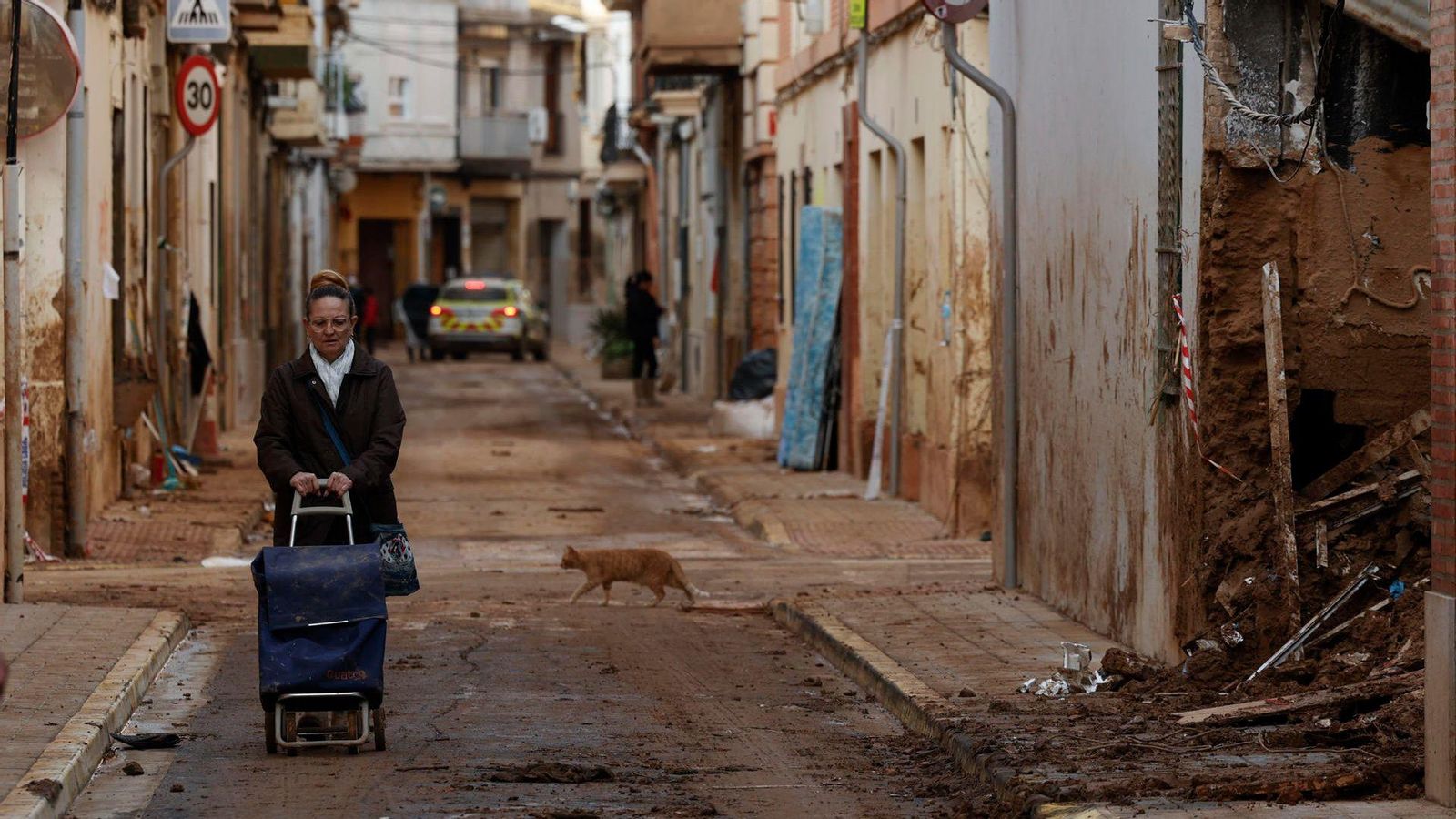 Una dona amb el carret de la compra avança per un carrer de Paiporta, amb empremptes evidents de la riuada