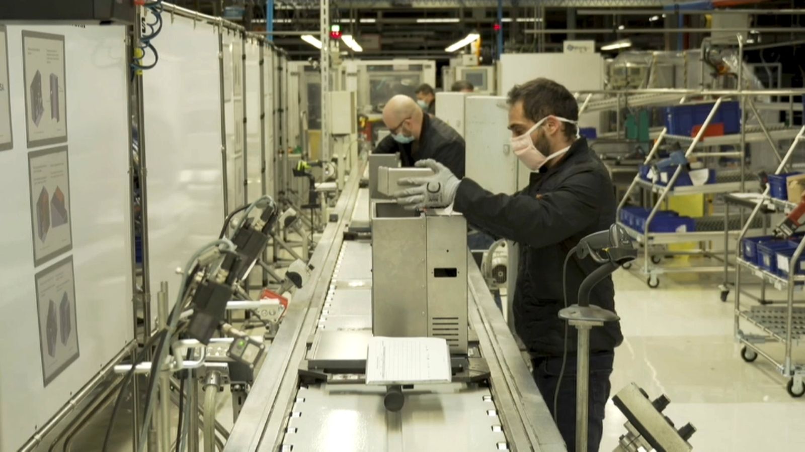 Treballadors d'una cadena de muntatge protegits amb màscares i guants en una imatge d'arxiu