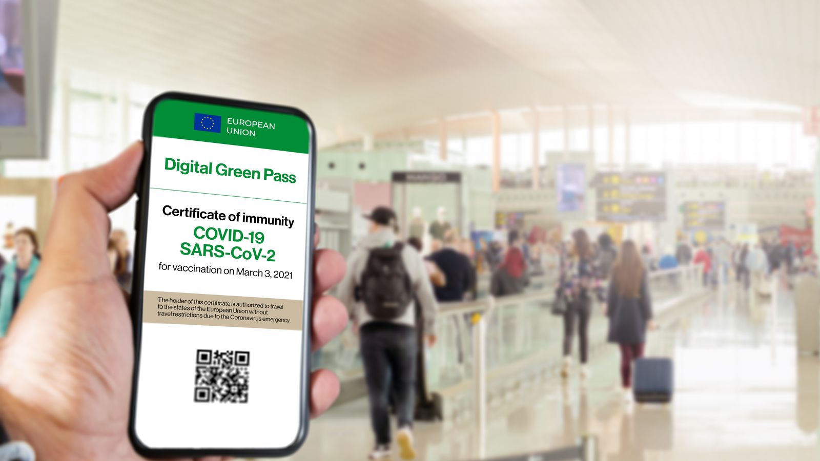 El certificat verd digital de la unió europea amb el codi QR en la pantalla d'un mòbil amb una mà amb un aeroport borrós en el fons. Immunitat de Covid-19. Viatjar sense restriccions.