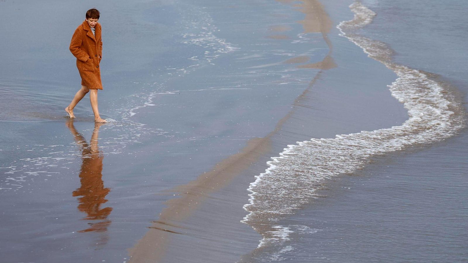 Una dona, amb abric, s'acosta a la vora de la mar de la platja de la Malva-rosa aprofitant les temperatures càlides dels últims dies