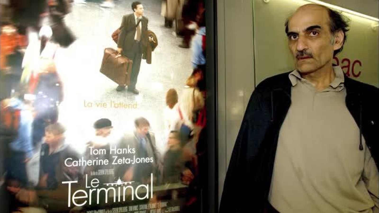 Mehran Karimi Nasseri, en qui es va inspirar producció d'Spielberg, en una imatge d'arxiu, juntament amb un cartell de la pel·lícula que va portar al cine la seua història