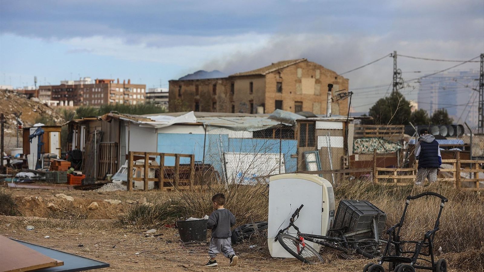 De fons, la columna de fum que va originar l'incendi declarat en l'assentament de xaboles a València