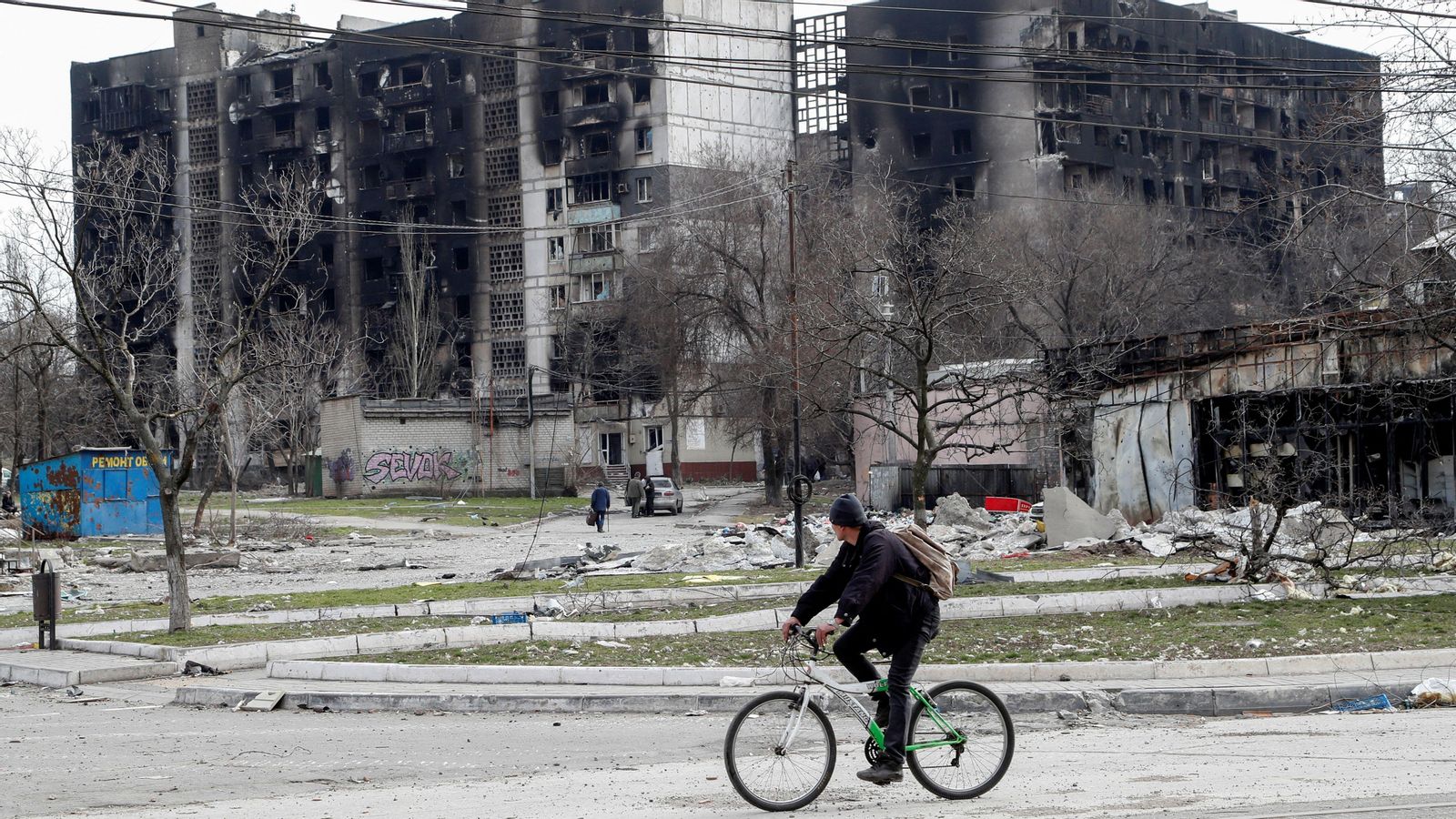 Un home va en bicicleta a prop d'uns edificis destruïts a Mariupol, Ucraïna