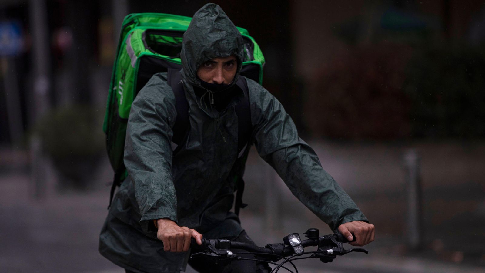 Imatge d’arxiu d’un repartidor que treballa sota la pluja, protegit amb un impermeable Imatge d’arxiu d’un rider que treballa sota la pluja, protegit amb un impermeable