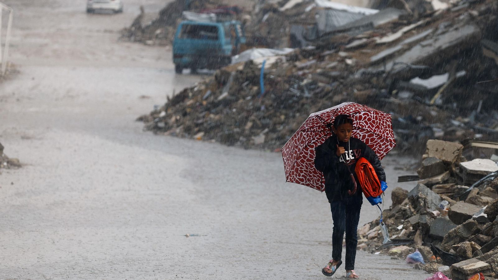 Un xiquet palestí avança, entre muntons de restes, un dia de pluja a Gaza, un dels territoris assotat per la guerra en els últims mesos