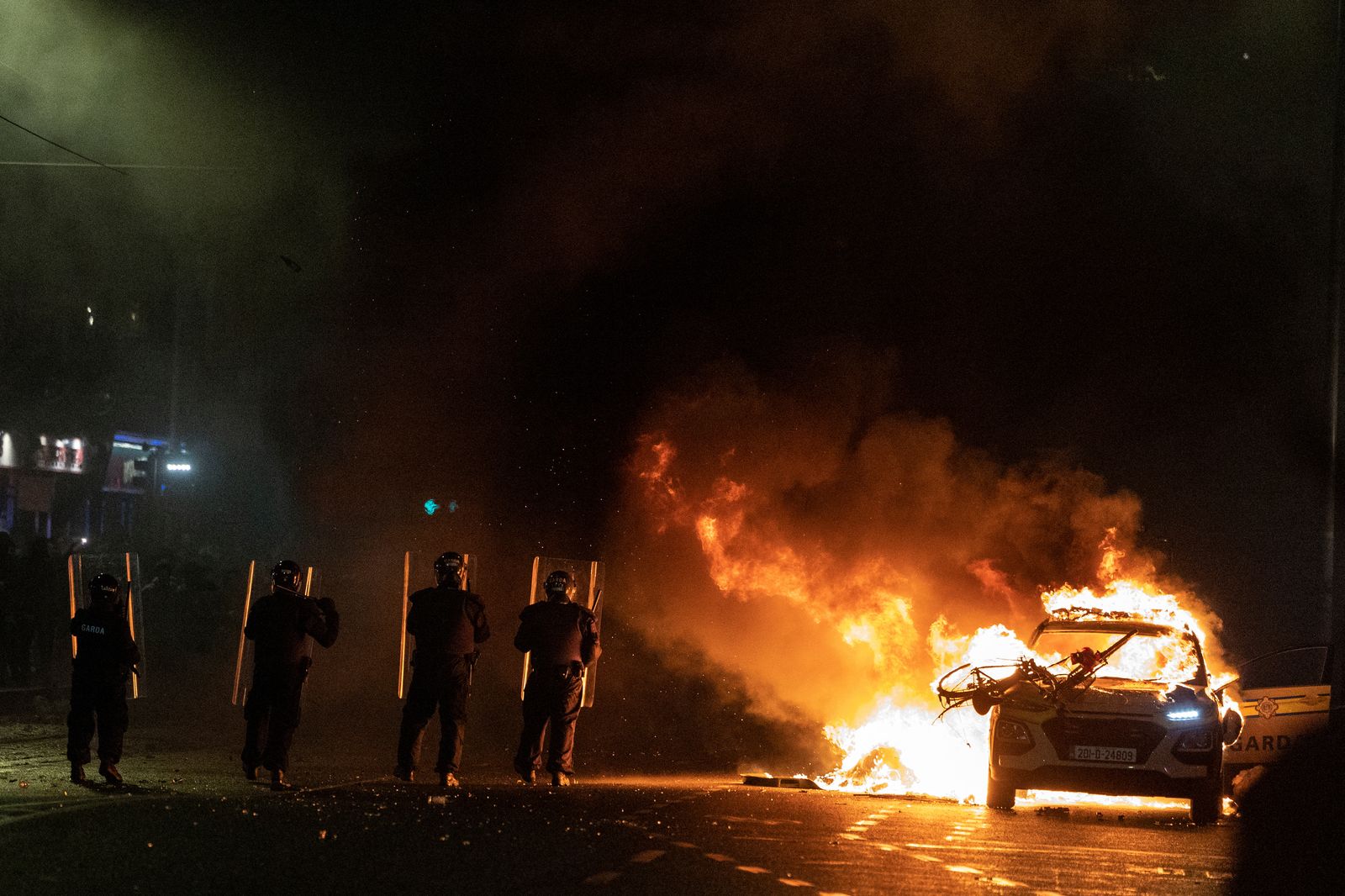 Agents antidisturbis s'enfronten als manifestants al costat d'un cotxe de policia en flames, a Dublín
