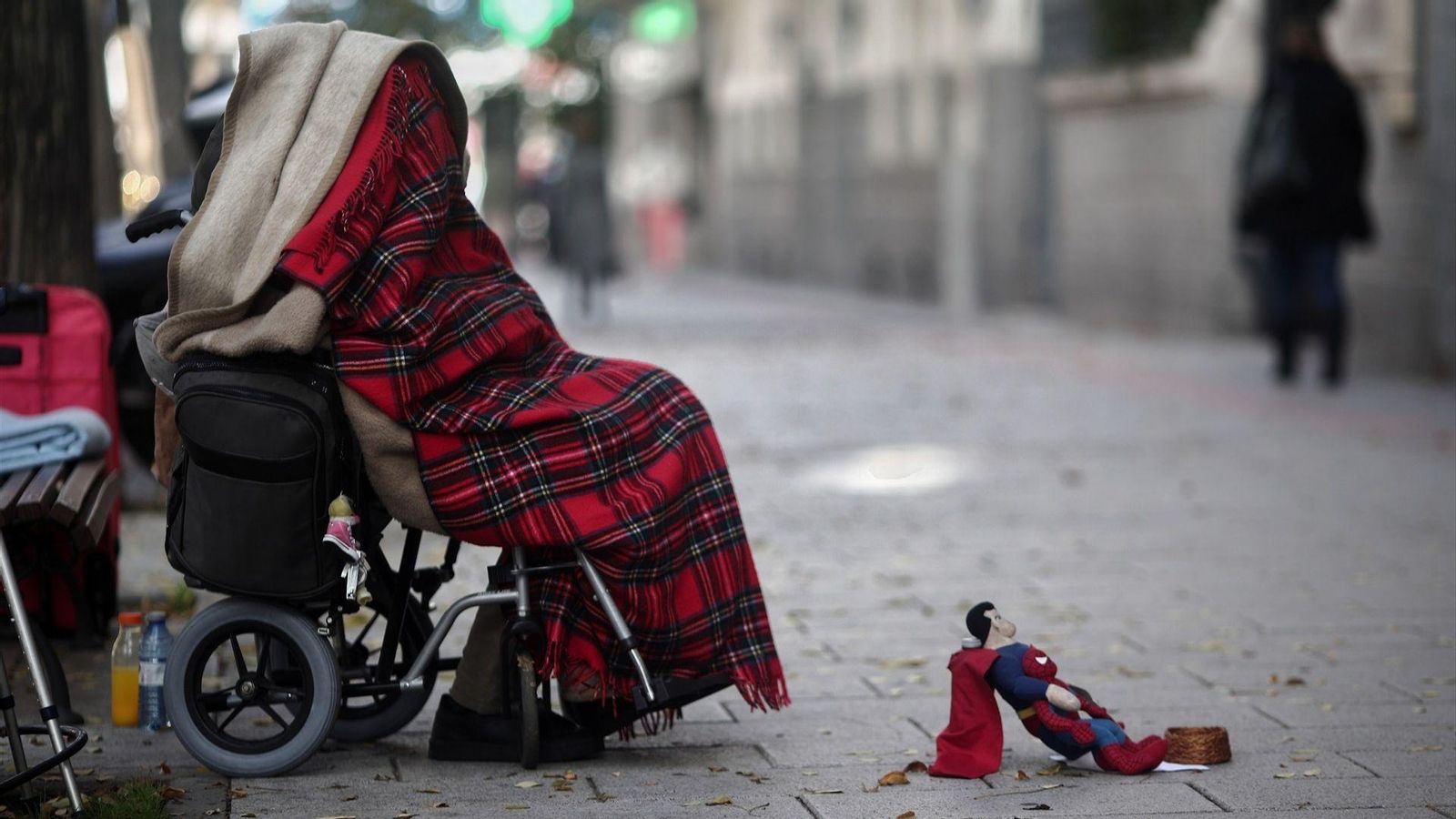 Imatge d'arxiu d'una persona en cadira de rodes tapada amb una manta demanant diners en el carrer