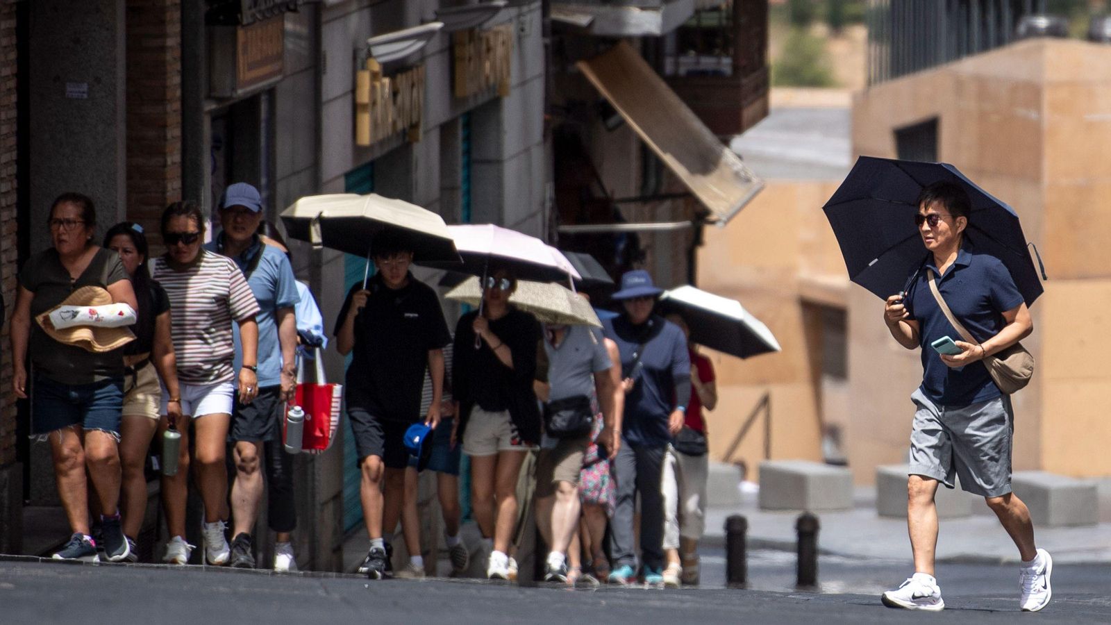 Un grup de turistes asiàtic es protegeixen amb paraigües mentre visiten Toledo, una de les ciutats que estarà aquest dimecres per damunt dels 40 graus