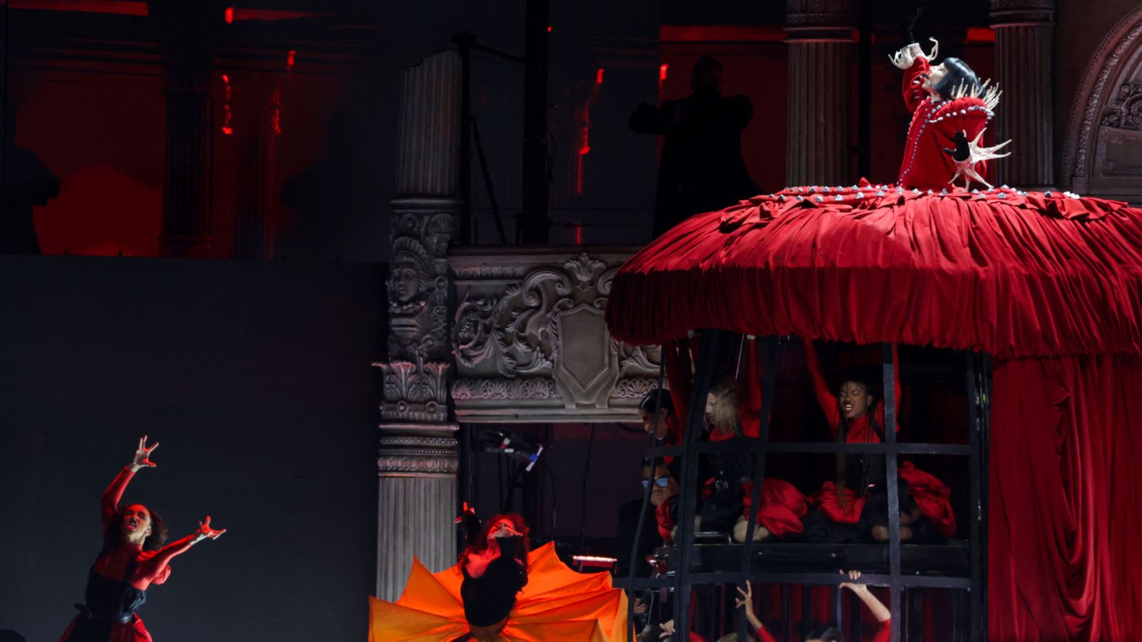 Lady Gaga, vestida amb un vibrant vestit roig, sobre una estructura victoriana