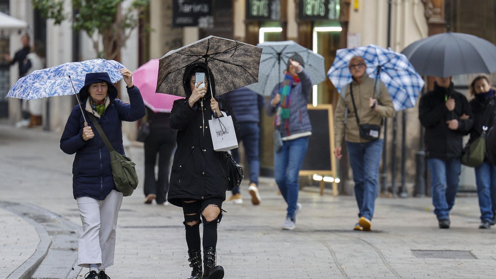 Diverses persones caminen pels carrers de València protegits de la pluja