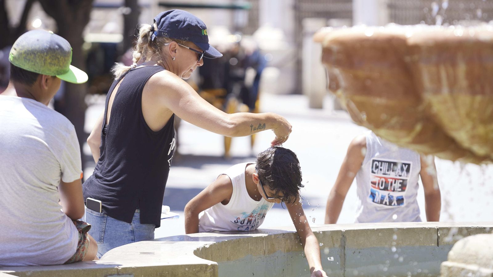 Una dona refreda el seu fill amb aigua en una font