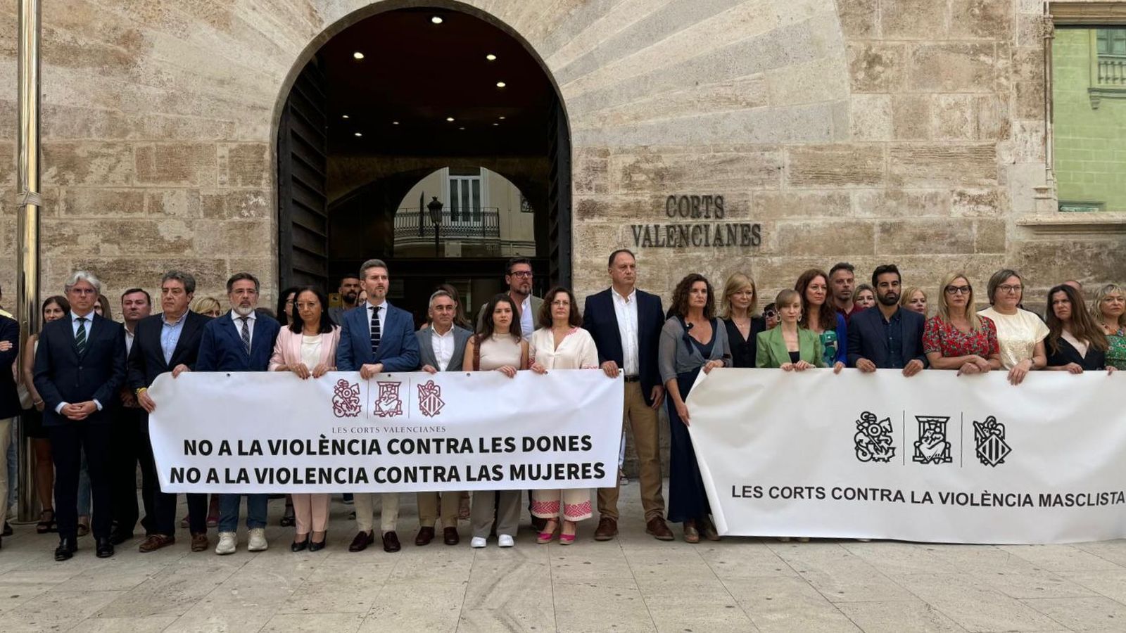 Minut de silenci davant de les Corts, amb dos pancartes: una contra la violència masclista i altra que diu no a la violència contra les dones