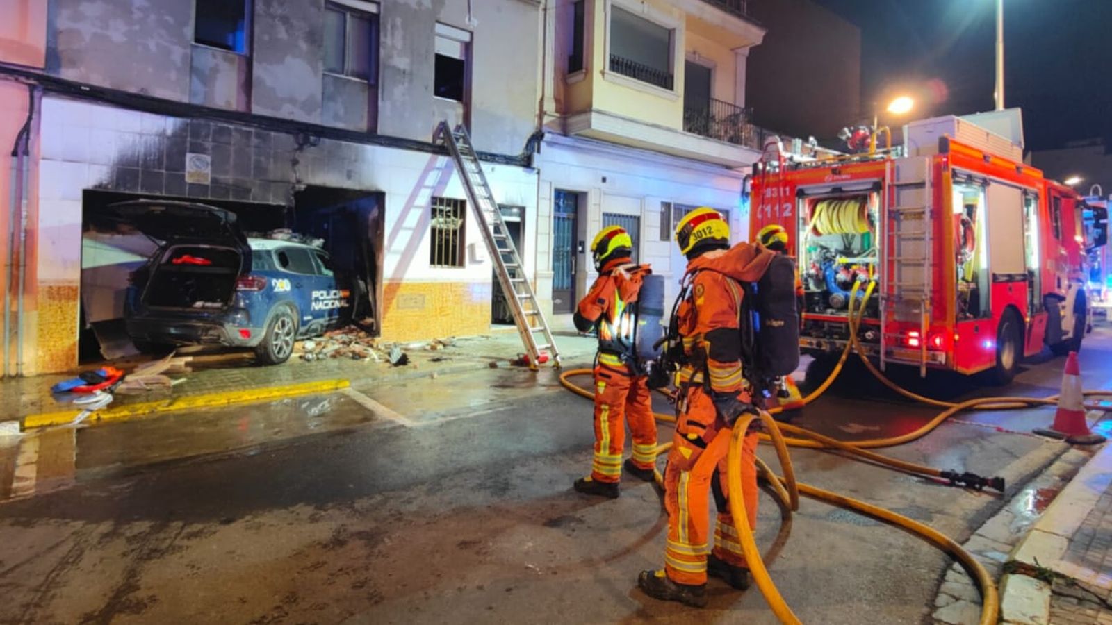 Els bombers treballen per a apagar les flames del cotxe policial incendiat