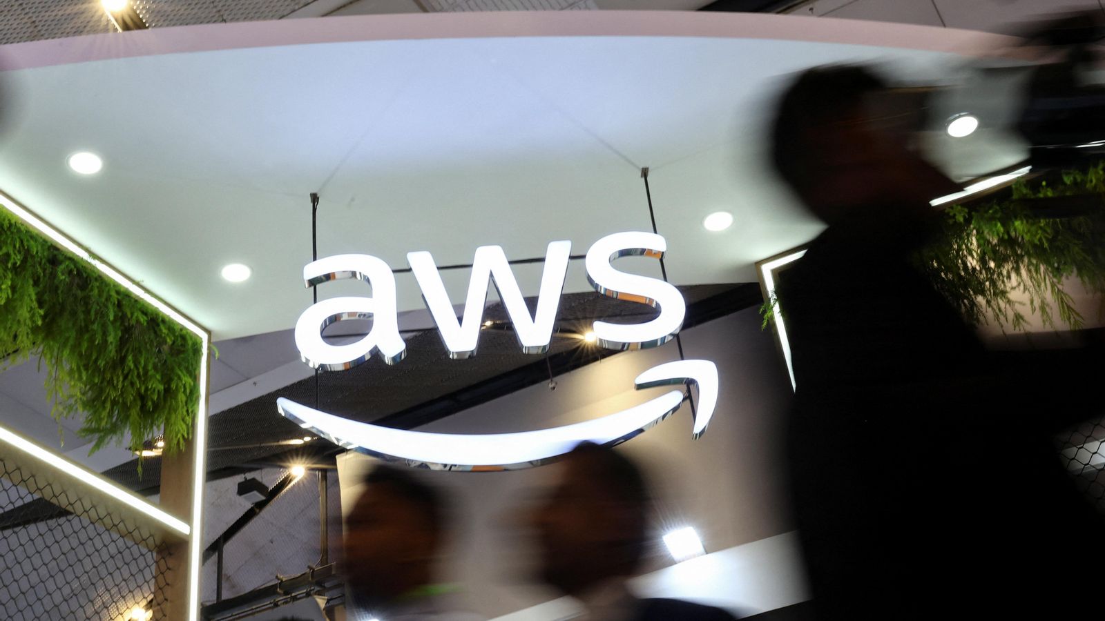 Diverses persones passen per davant del logo d'AWS en una convenció a Nova Delhi, l'Índia Diverses persones passen per davant del logo d'AWS en una convenció a Nova Delhi, l'Índia