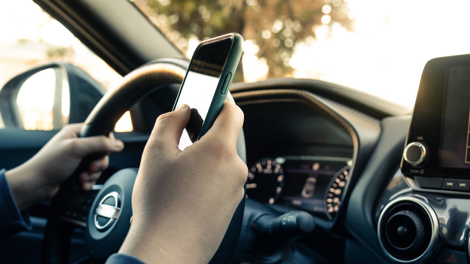 Una persona mira el mòbil mentre condueix