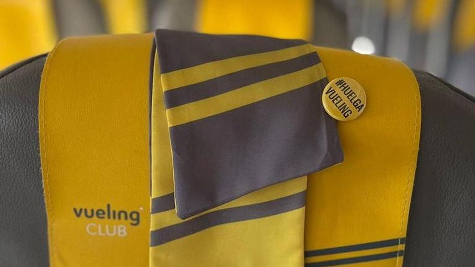 Mocador d'una tripulant de cabina de Vueling en un seient de l'avió amb un pin de la vaga