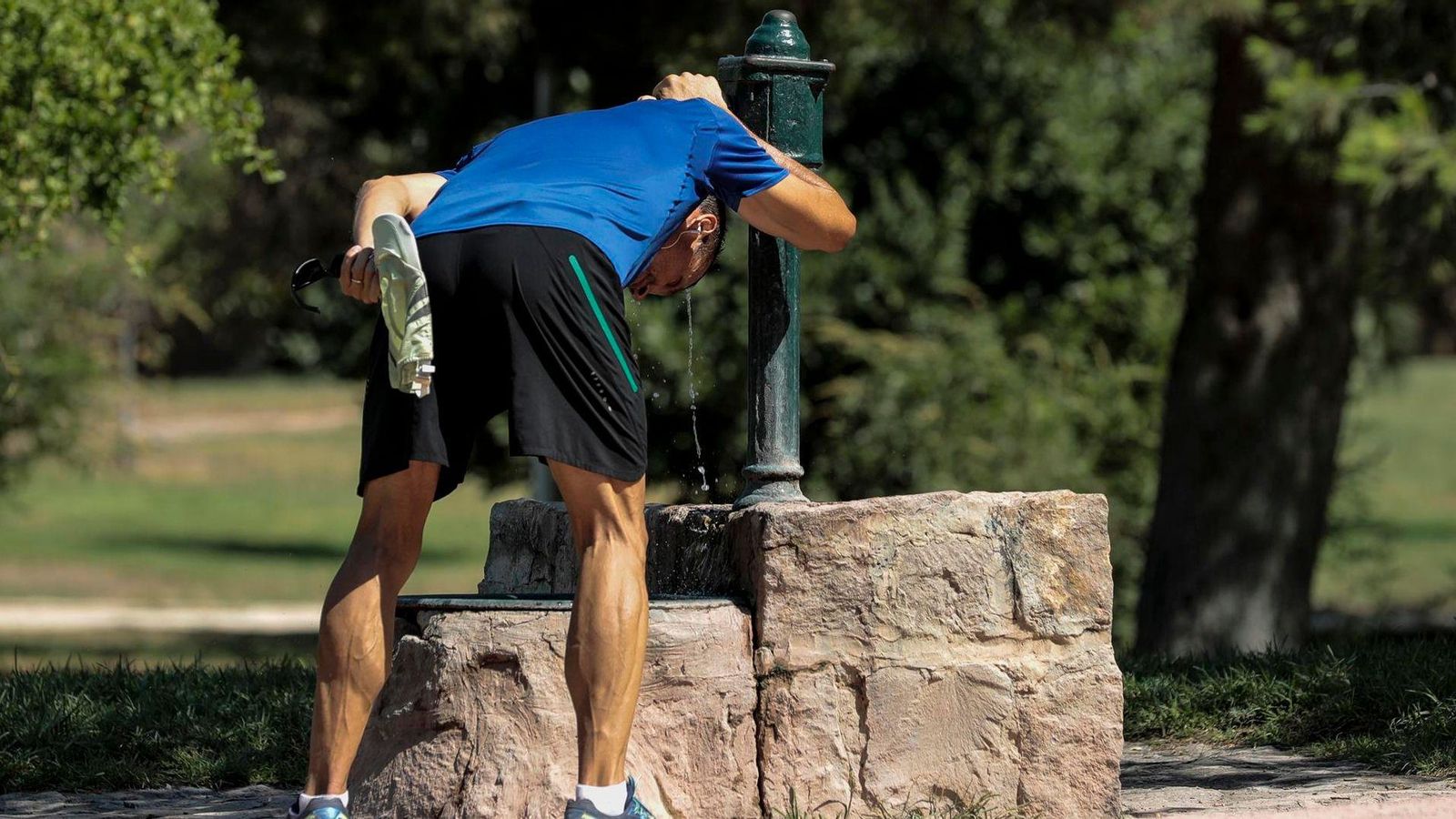 Un corredor es refresca en una font del Jardí del Túria de la ciutat de València
