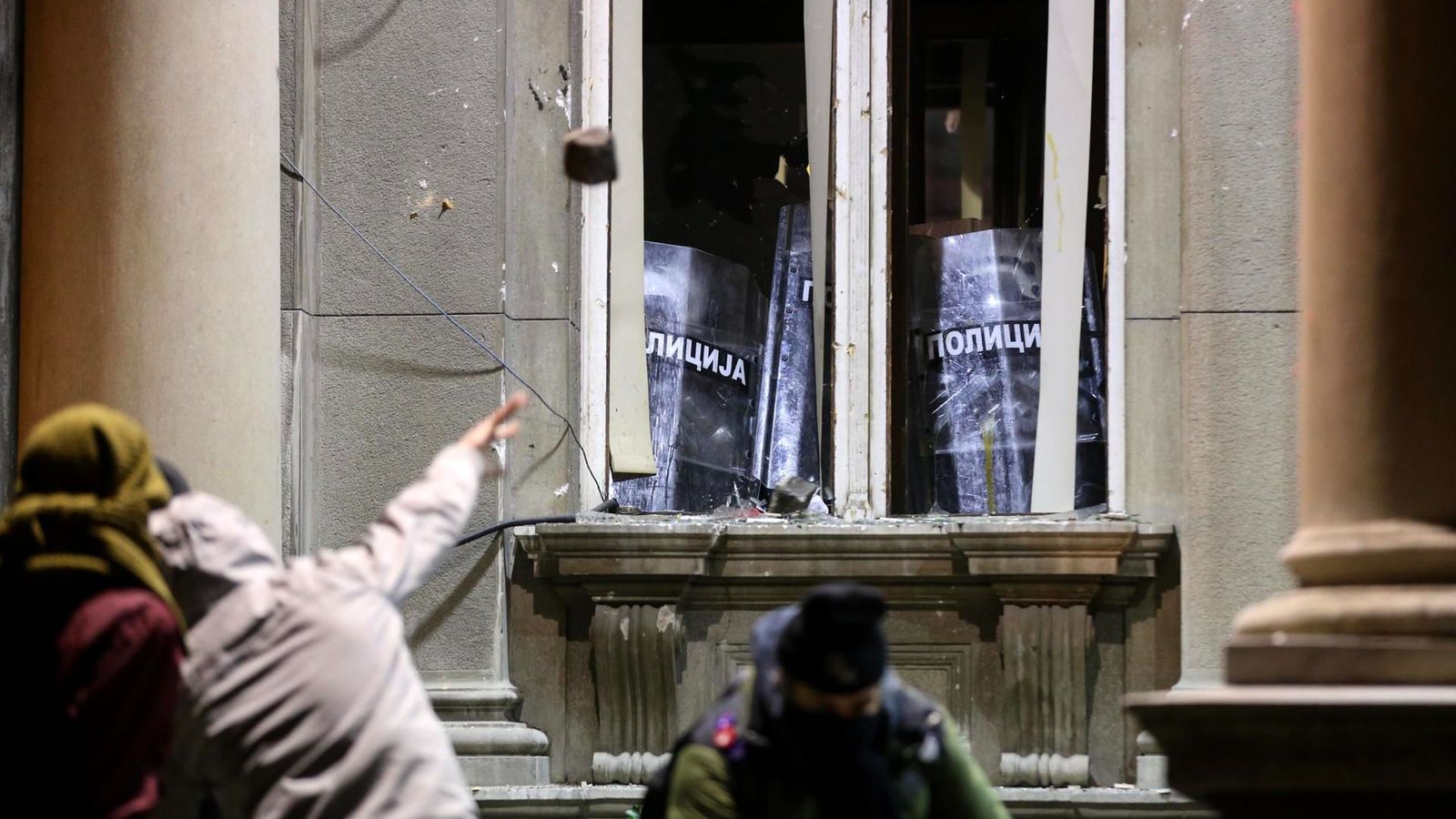Un manifestant llança una pedra a una finestra de l'ajuntament, darrere de la qual es protegeixen diversos policies amb escuts de protecció