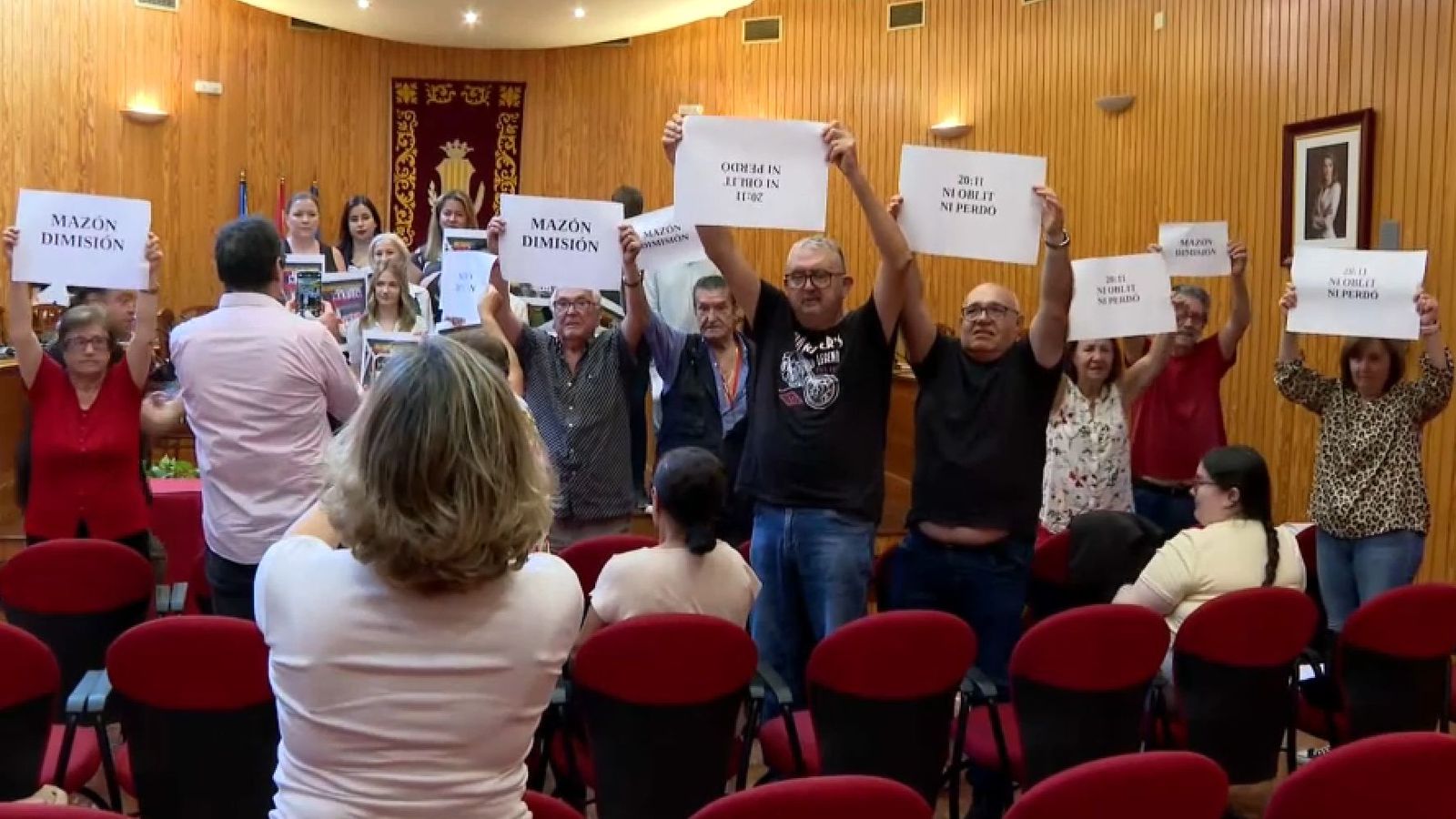 Un grup de veïns contraprograma amb cartells de "Mazón dimissió" (davant) i les pancartes de l'oposició (al fons) reclamen l'eixida del regidor de Seguretat, en el ple municipal