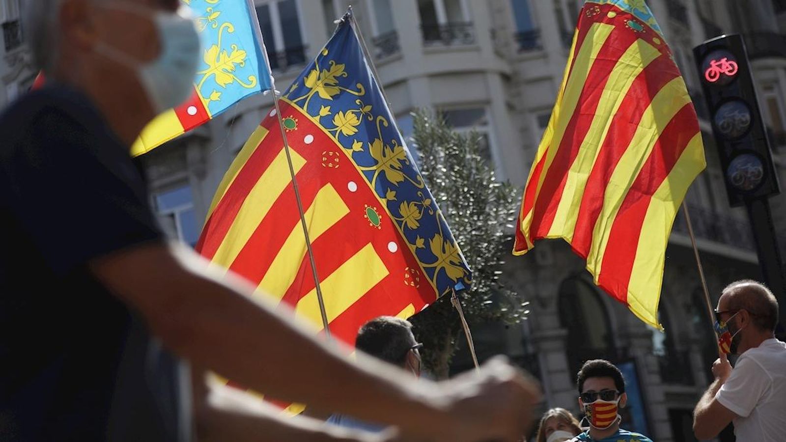 Diverses persones onegen la bandera valenciana baix de l'Ajuntament de València en el moment en què se celebrava un acte d'homenatge institucional i ciutadà a la Senyera en substitució de la tradicional processó cívica, que enguany no s'ha celebrat a causa de la pandèmia de coronavirus