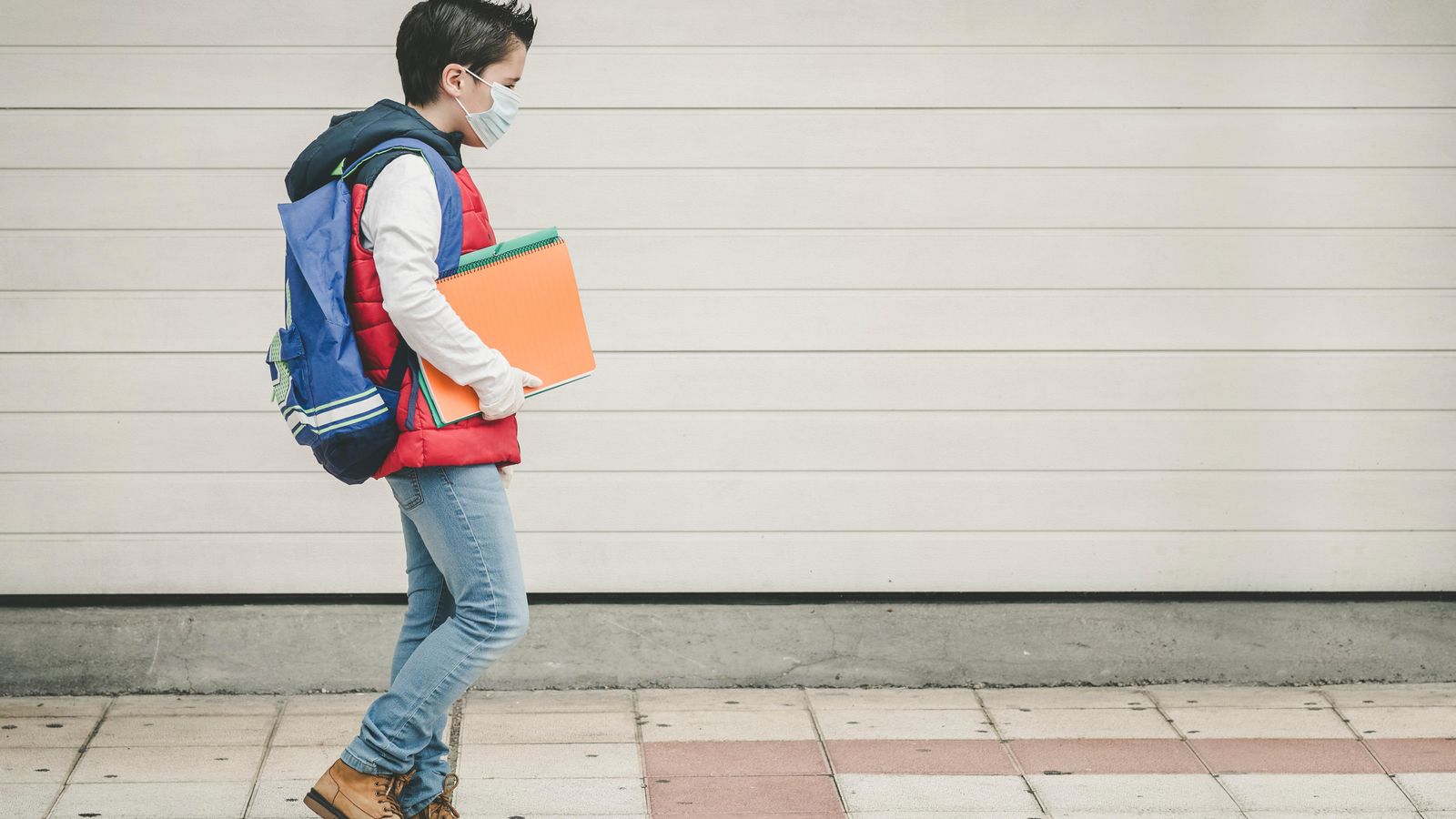 Un xiquet amb mascareta camina cap a una escola en una imatge d'arxiu