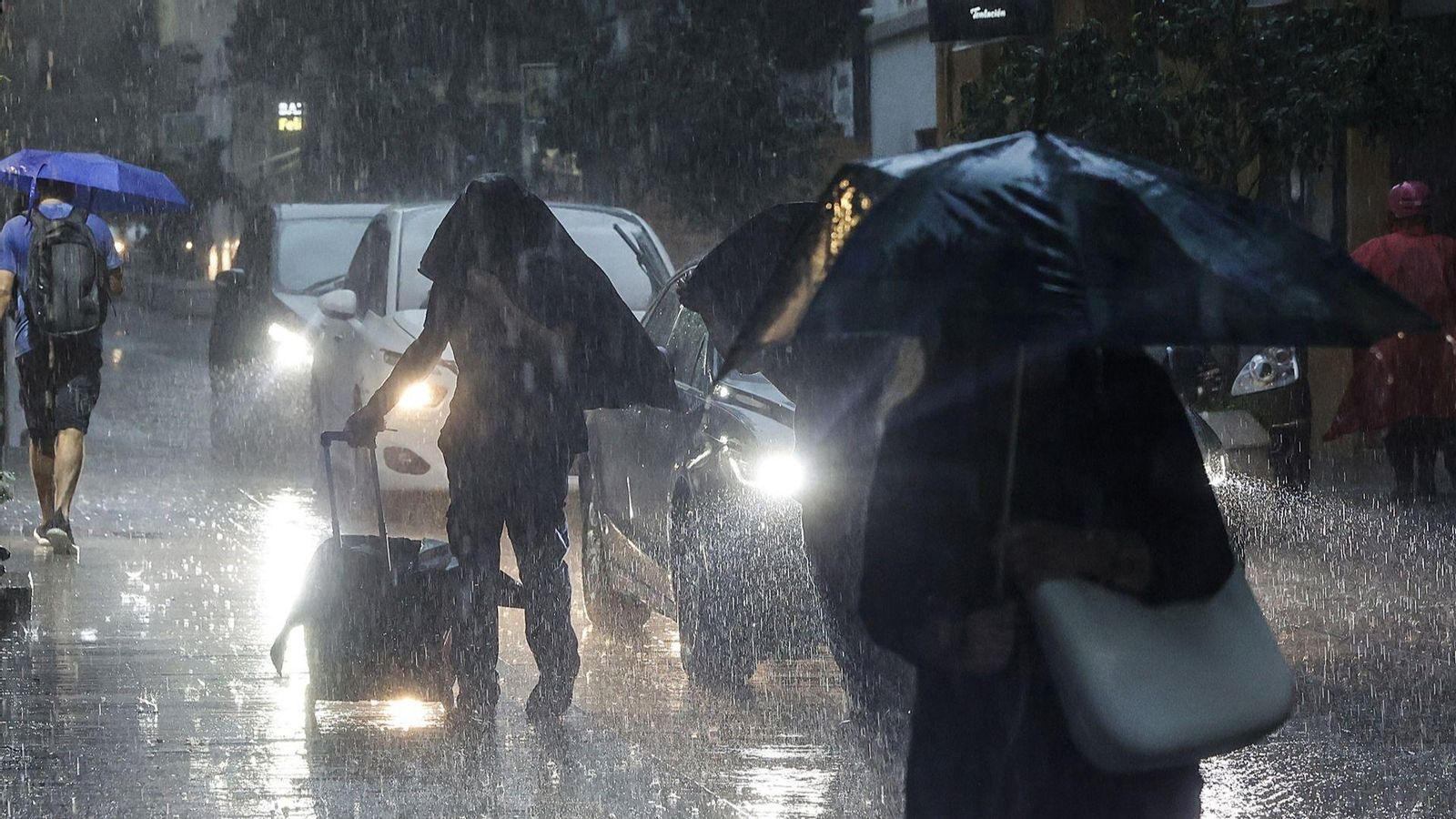 Diverses persones amb motxilles i maletes caminen baix la pluja (arxiu)