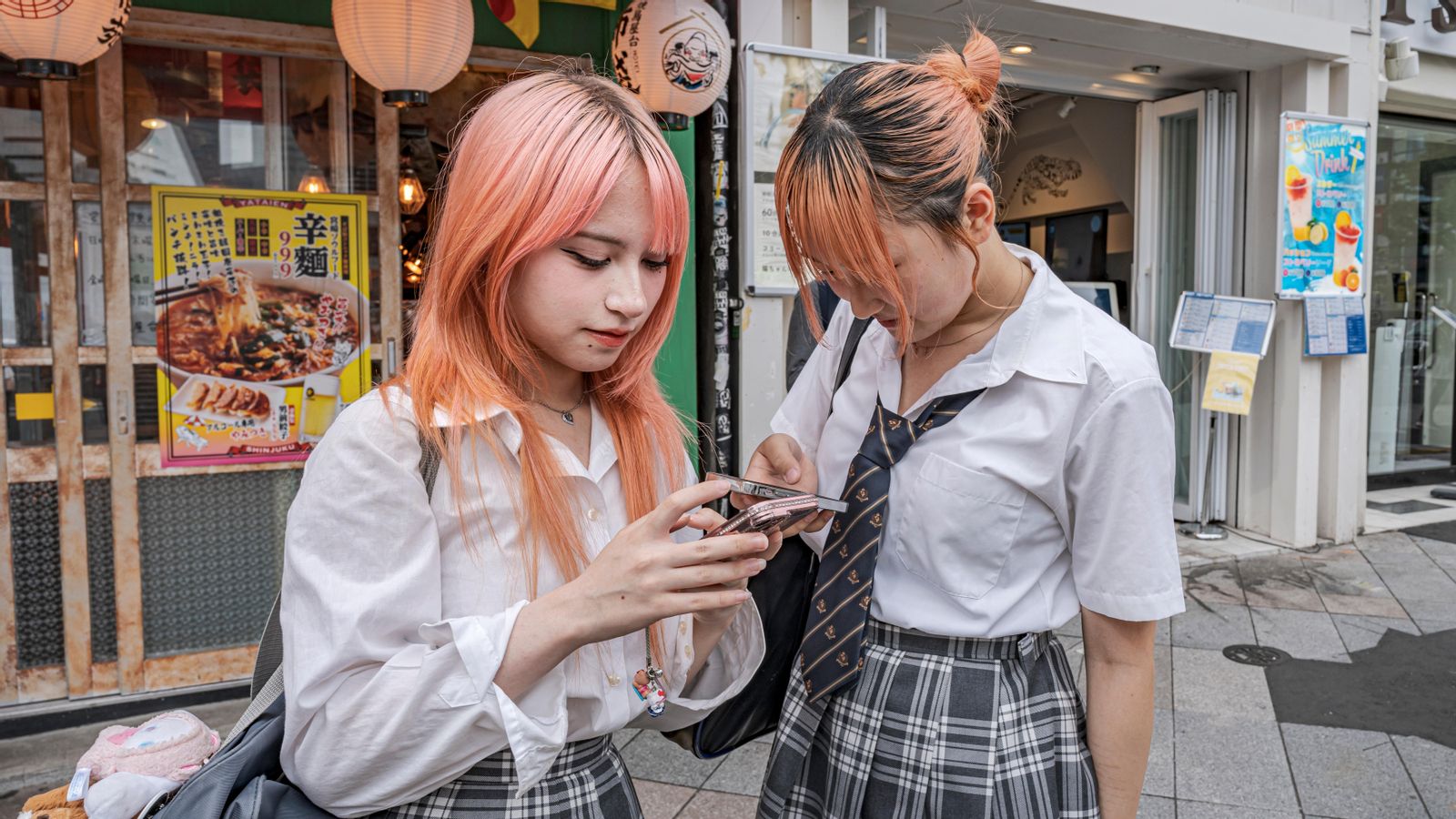 Estudiants de secundària japoneses amb el pèl tenyit de rosa miren els seus telèfons intel·ligents.