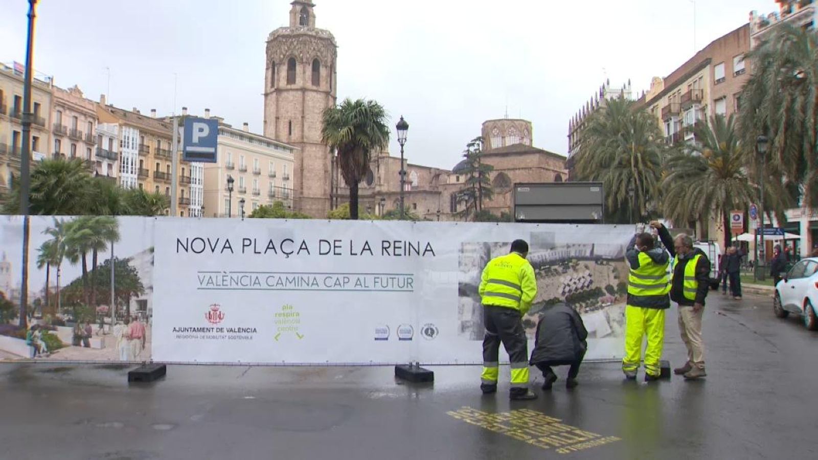 Uns operaris alcen el cartell que informa de les obres de la Plaça de la Reina