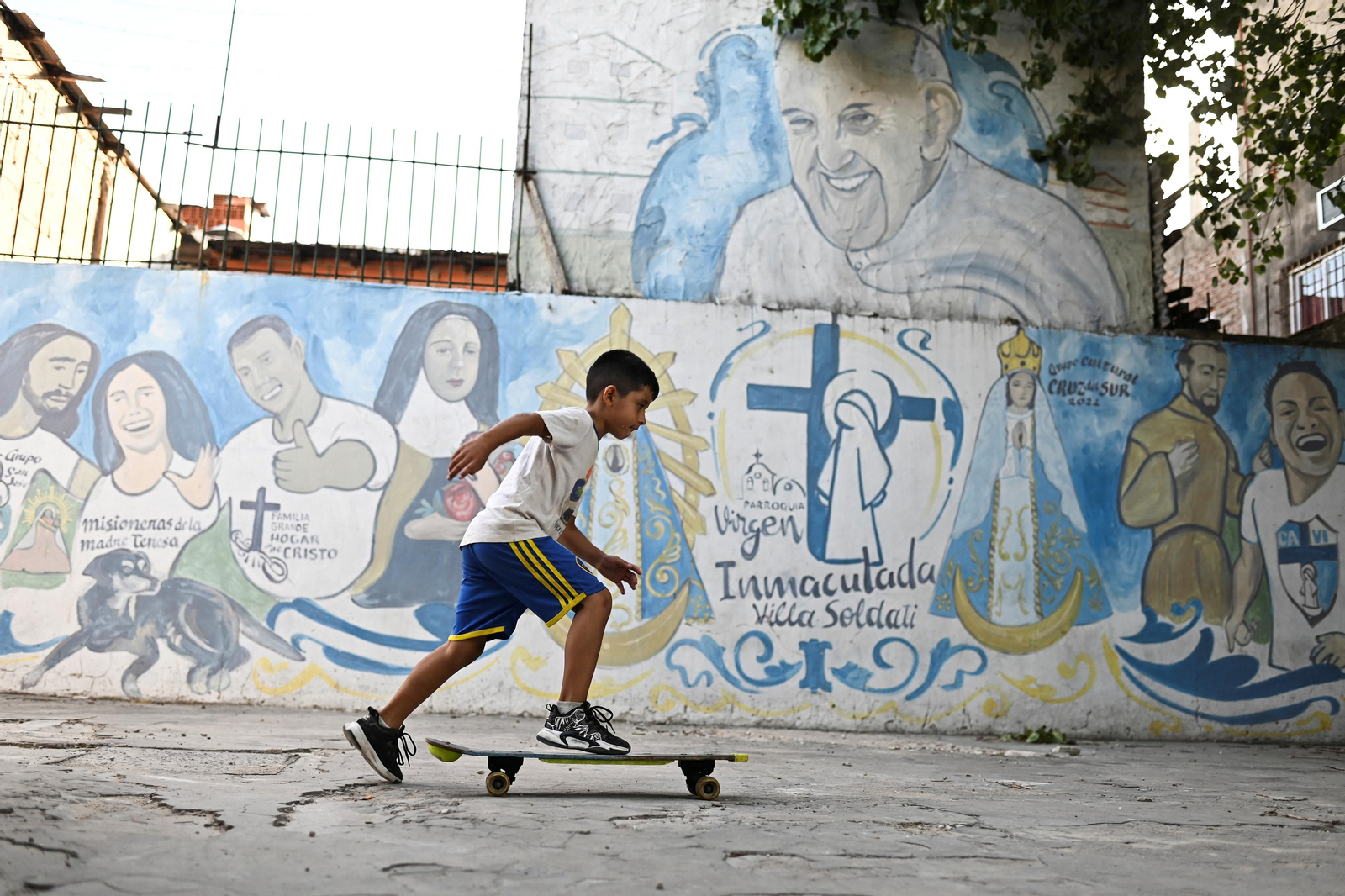 Un xiquet passa amb un patinet davant d'un mural del papa a Buenos Aires