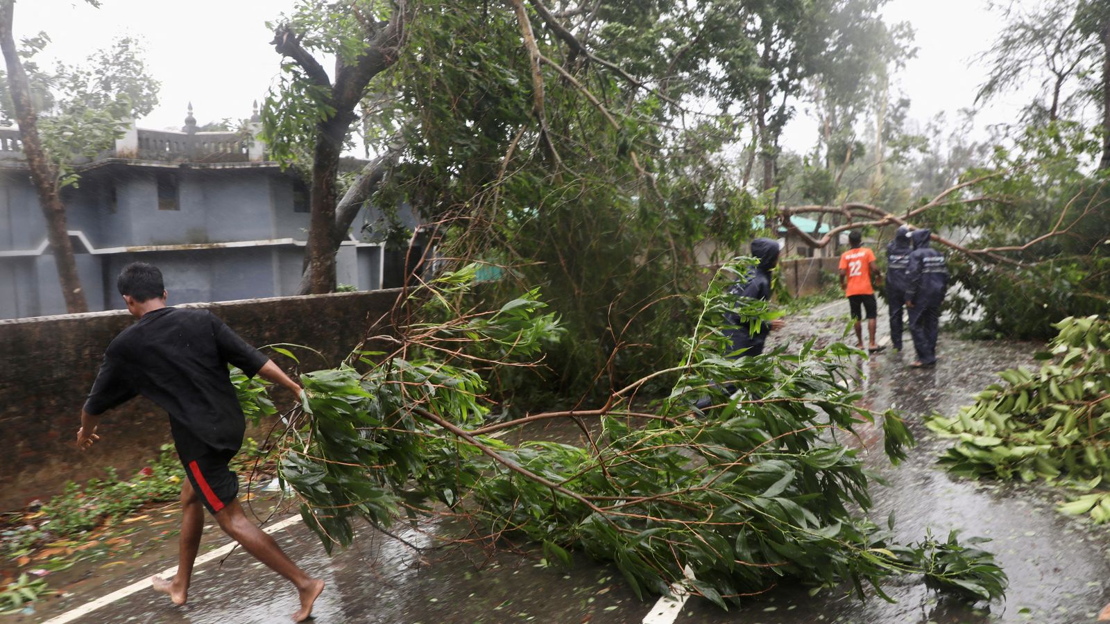 La gent mou arbres caiguts des d'una carretera a després de la caiguda del cicló Mocha a Teknaf, Bangladesh