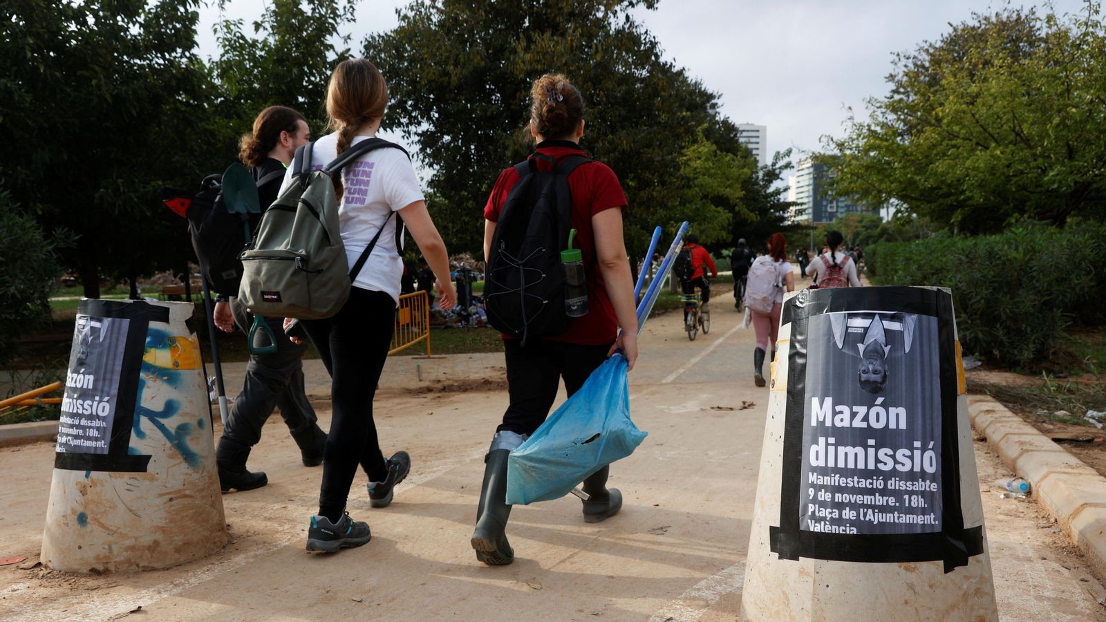 Persones voluntàries caminen al costat de cartells que convoquen a la manifestació sota el lema "Mazón dimissió" a València Cartells que convoquen a la manifestació sota el lema "Mazón dimissió" a València, amb una imatge del president cap per avall