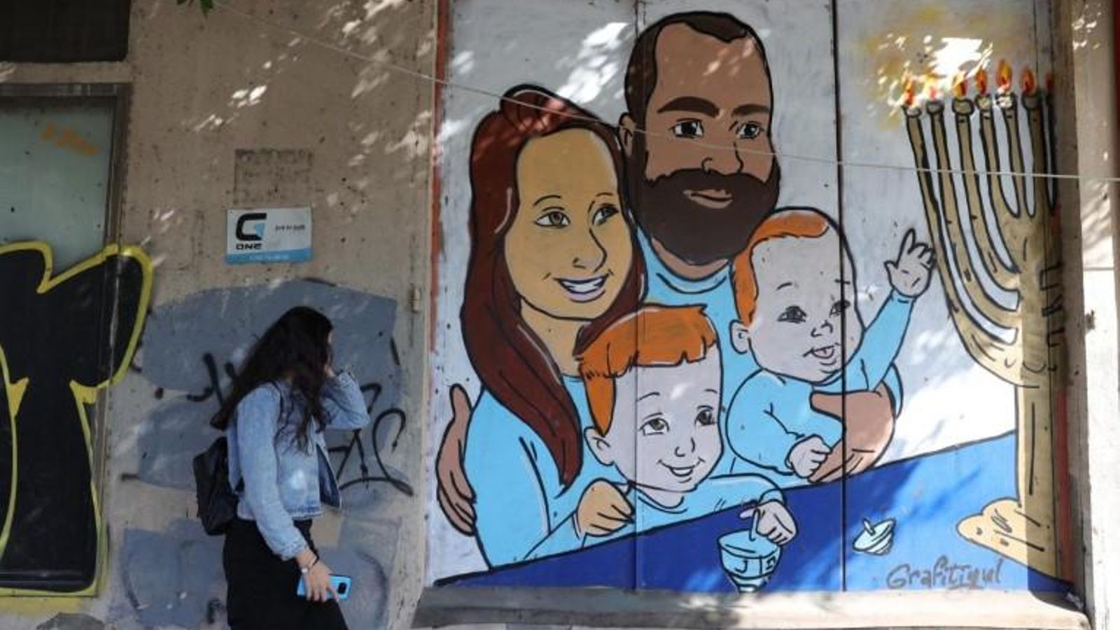 Una dona passa al costat d'un grafiti de la família Bibas a Tel Aviv, Israel, este dijous