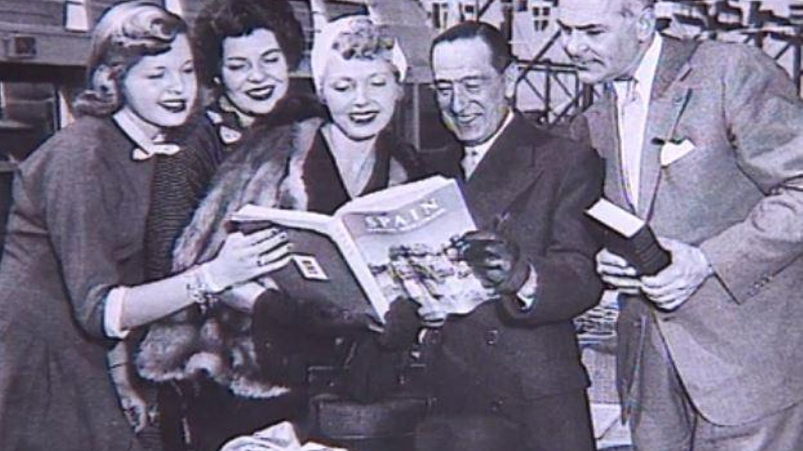 Imatge publicitaria d'un grup de persones estrangeres llegint una revista dedicada a Espanya