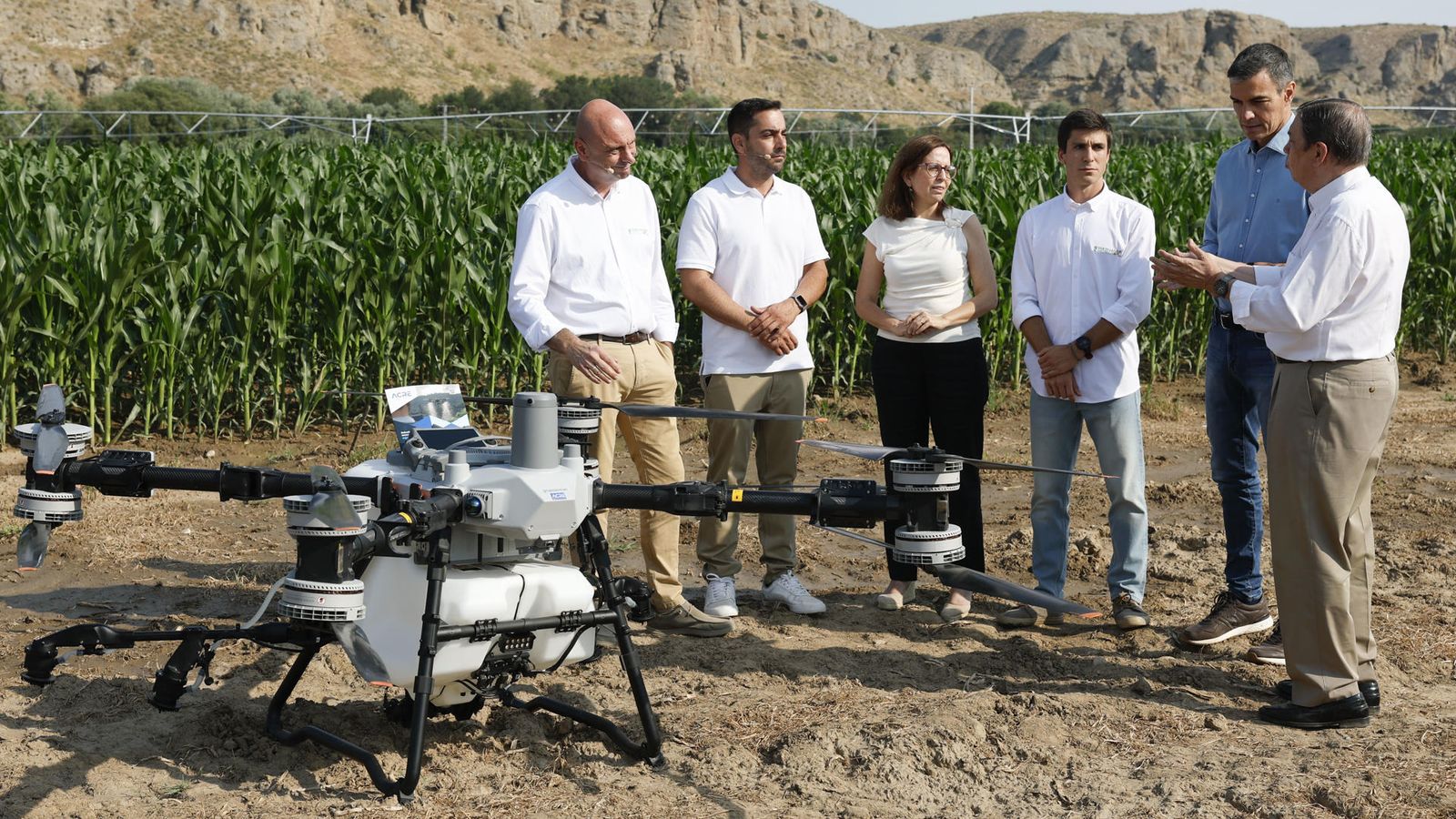 El president del govern espanyol i el ministre d'Agricultura conversen davant un dron preparat per a llançar fertilitzants junt a un camp de dacsa