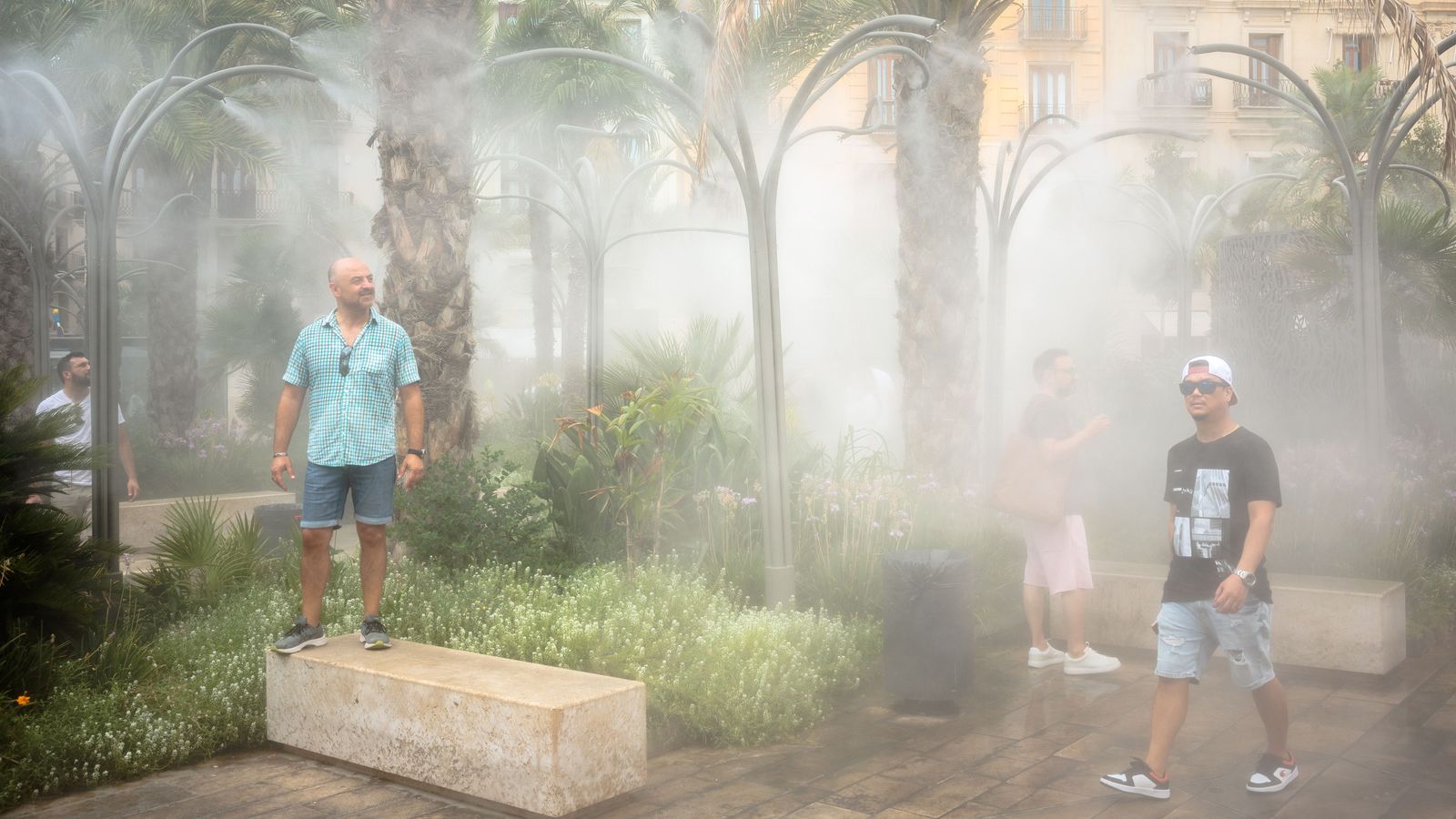 Diverses persones es refresquen baix les fonts de la Plaça de la Rèina, a València