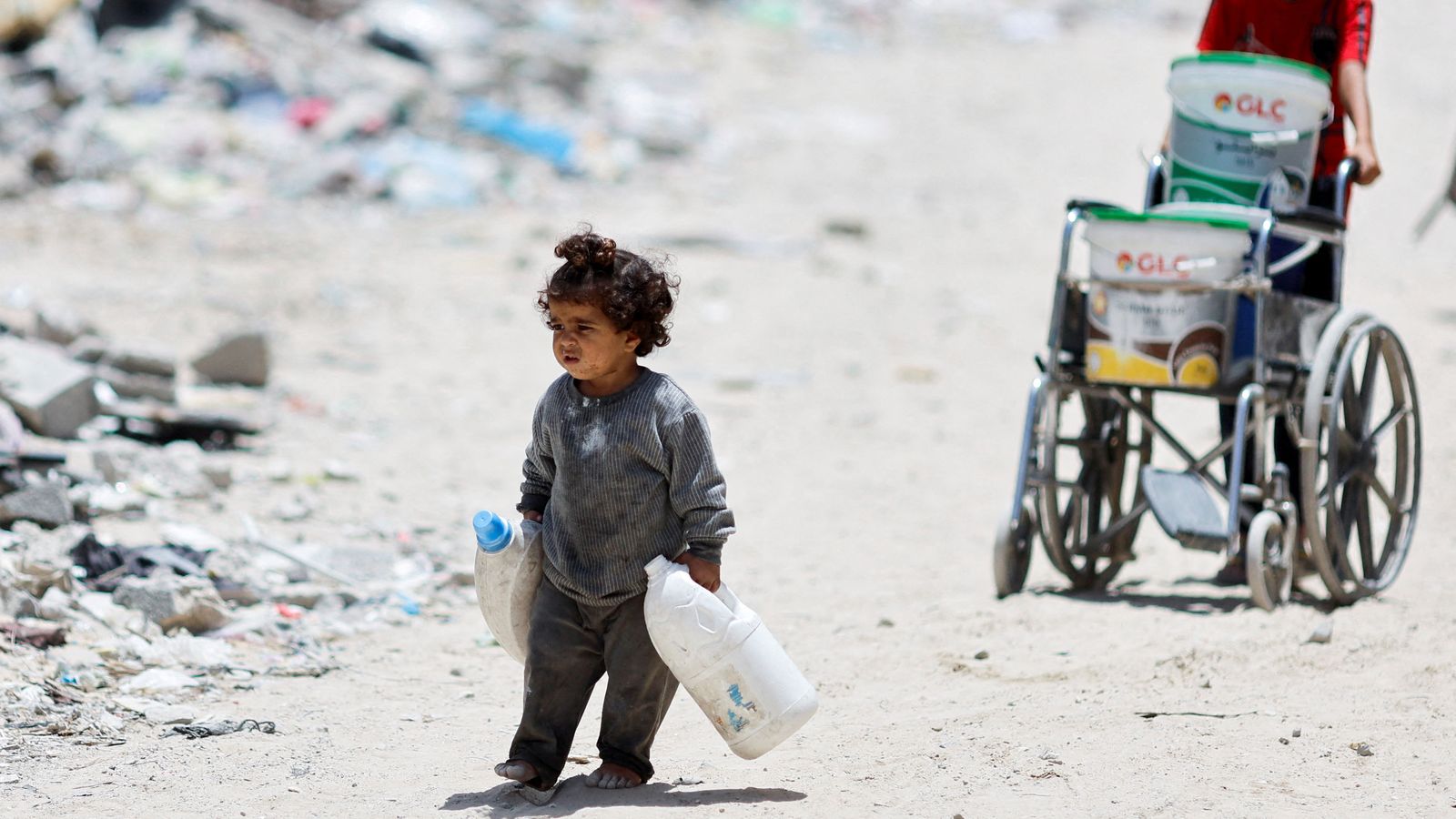 Uns xiquets palestins caminen entre enderrocs, de camí a una de les cues d'aliments de Khan Younis